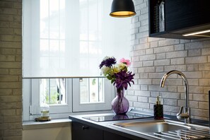 Una cocina con ventana, un lavamanos, un jarrón con flores y una lámpara colgante.