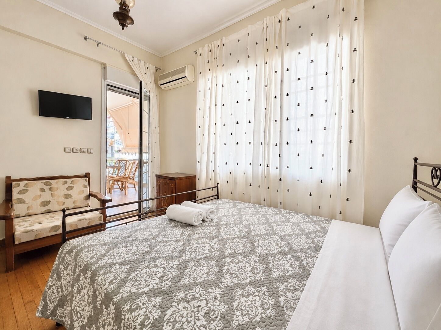 Une chambre à coucher avec un lit, une chaise, un téléviseur et une fenêtre avec des rideaux.