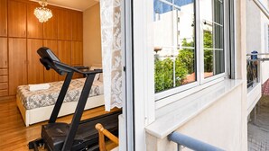 Un dormitorio con una caminadora, una cama, un armario de madera y una ventana con vistas a zonas verdes.