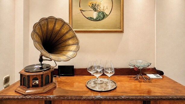A wooden table with a gramophone, a framed botanical painting, and a tray with wine glasses.
