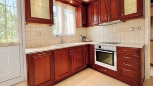 A kitchen with wooden cabinets, a white countertop, a stove, and a window with curtains.