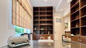 Una habitación con una máquina de escribir sobre una mesa de mármol, un armario de madera con estantes y una puerta que da a otra habitación.