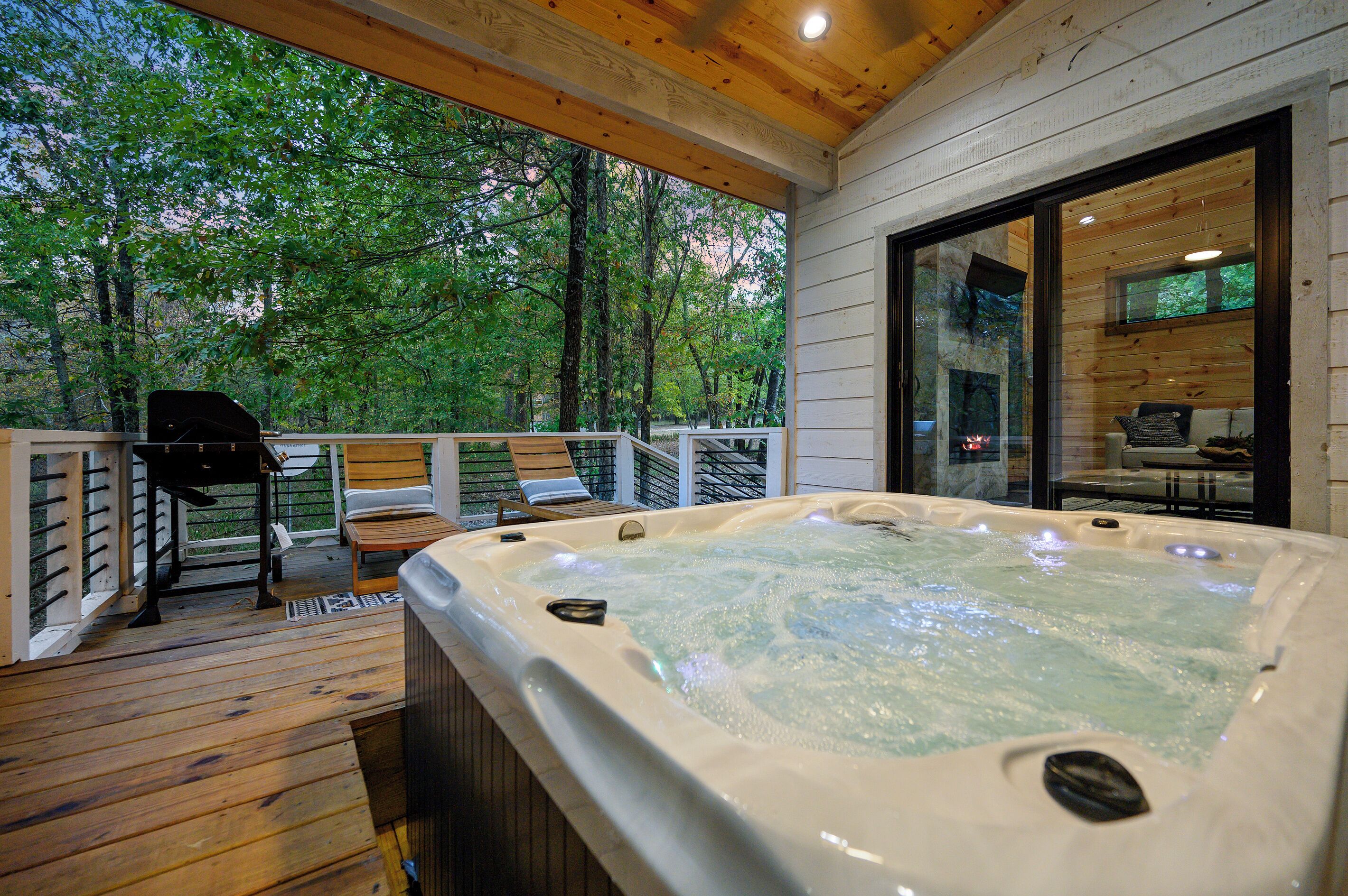 Ein Whirlpool auf einer Holzterrasse mit einem gläsernen Raum und Blick auf Bäume.