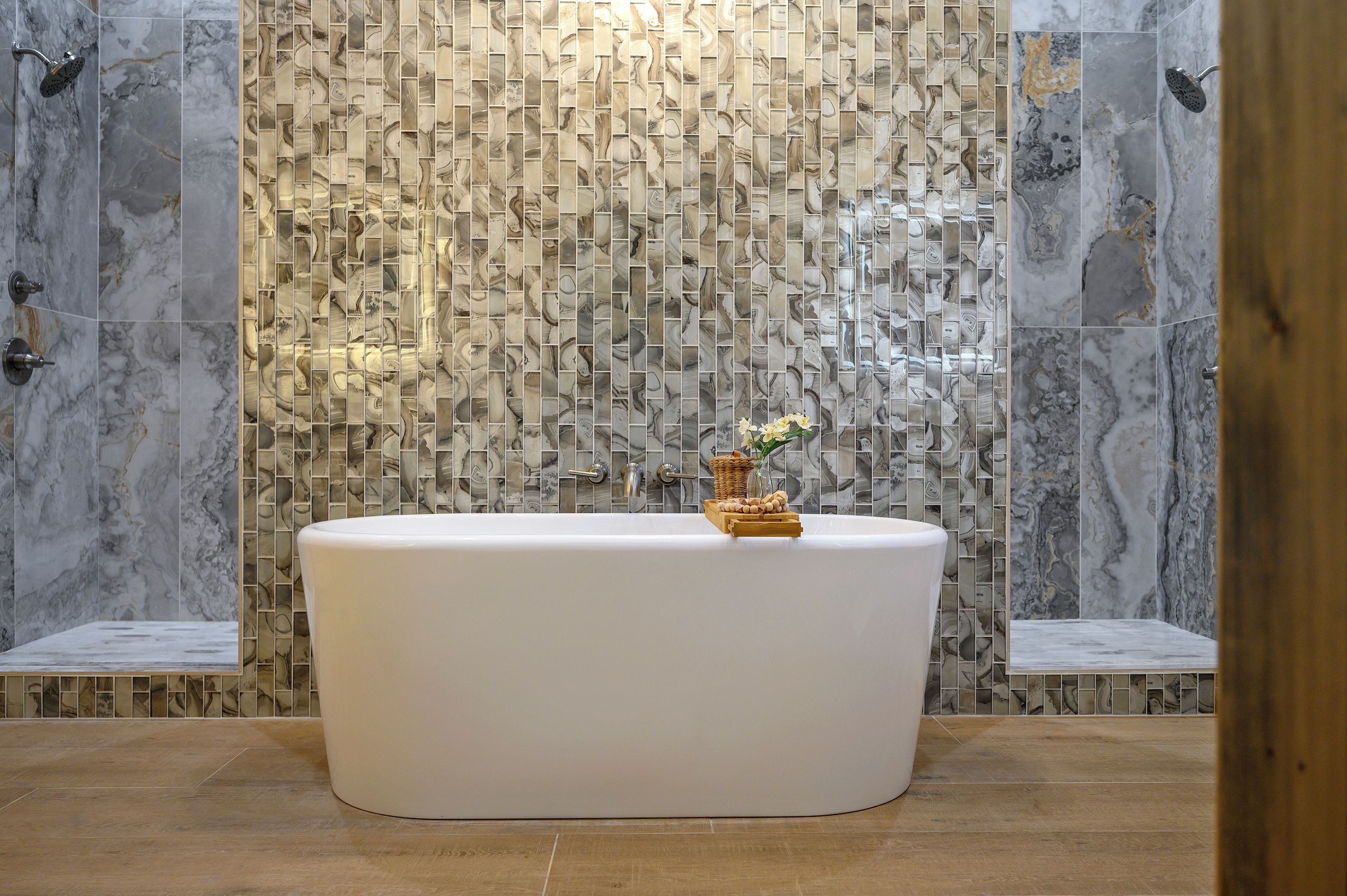 Ein Badezimmer mit freistehender Badewanne, Marmorfliesen an den Wänden und Holzboden.