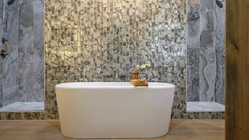 Ein Badezimmer mit freistehender Badewanne, Marmorfliesen an den Wänden und Holzboden.