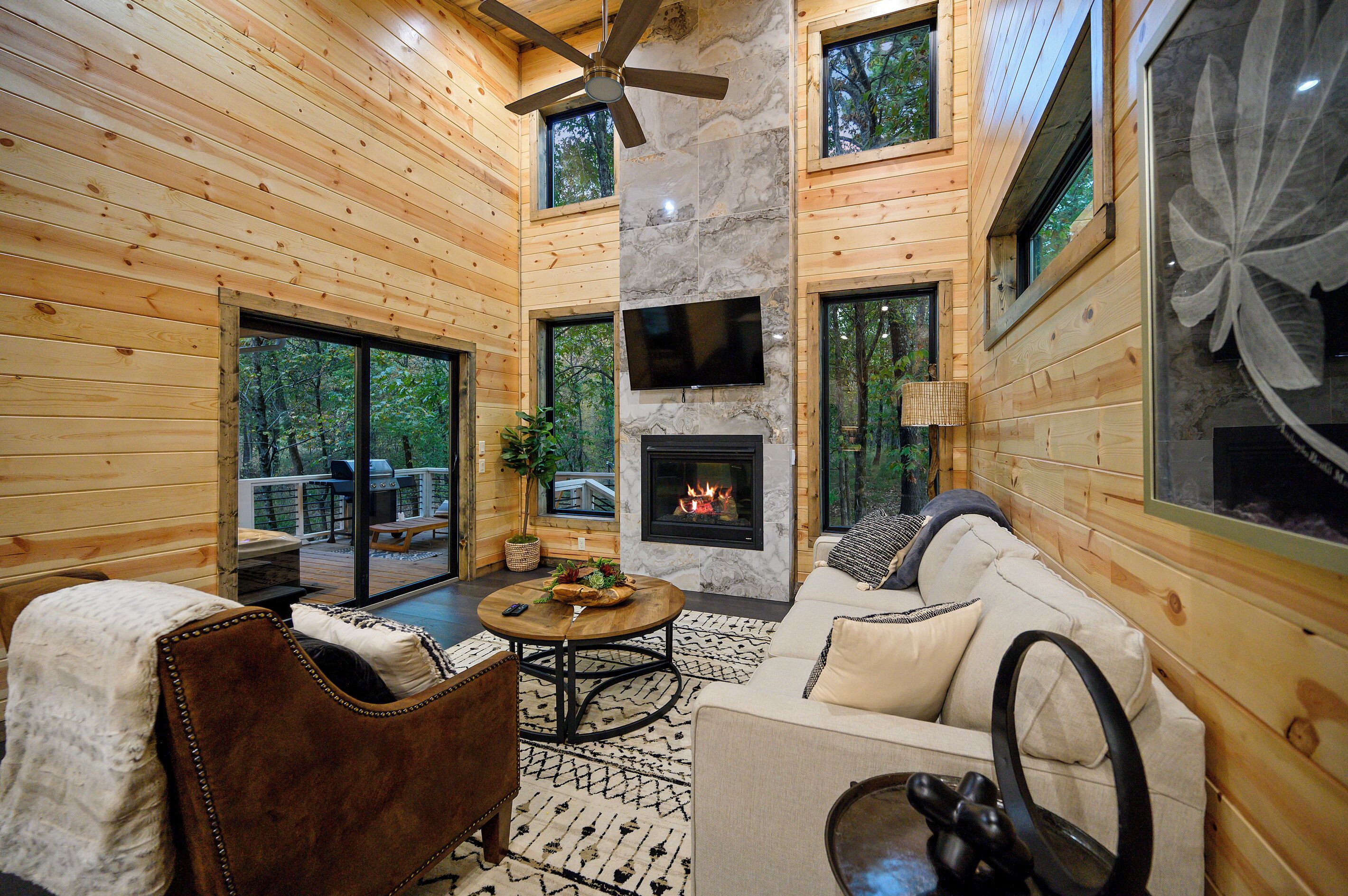 Un interior de cabaña acogedor, con chimenea, paredes de madera y ventilador de techo.
