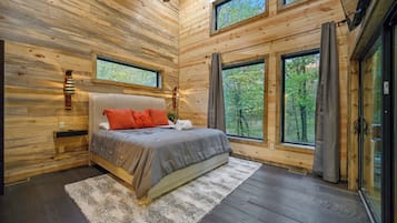 Une chambre dans une cabane en bois, avec un lit, des fenêtres et un ventilateur de plafond.