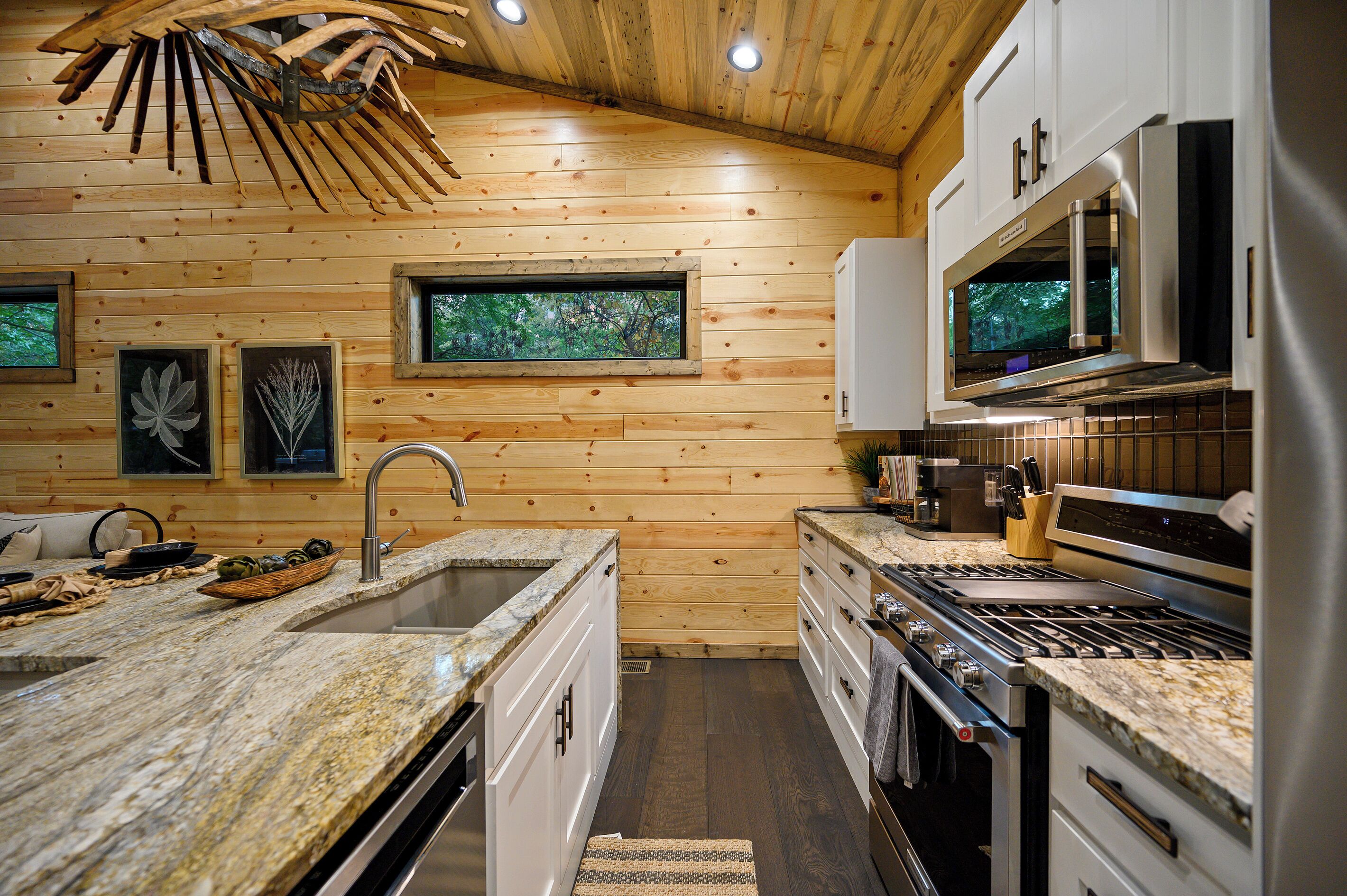 Una cocina moderna con paredes de madera, encimera de granito, electrodomésticos de acero inoxidable y una ventana con vistas a árboles.