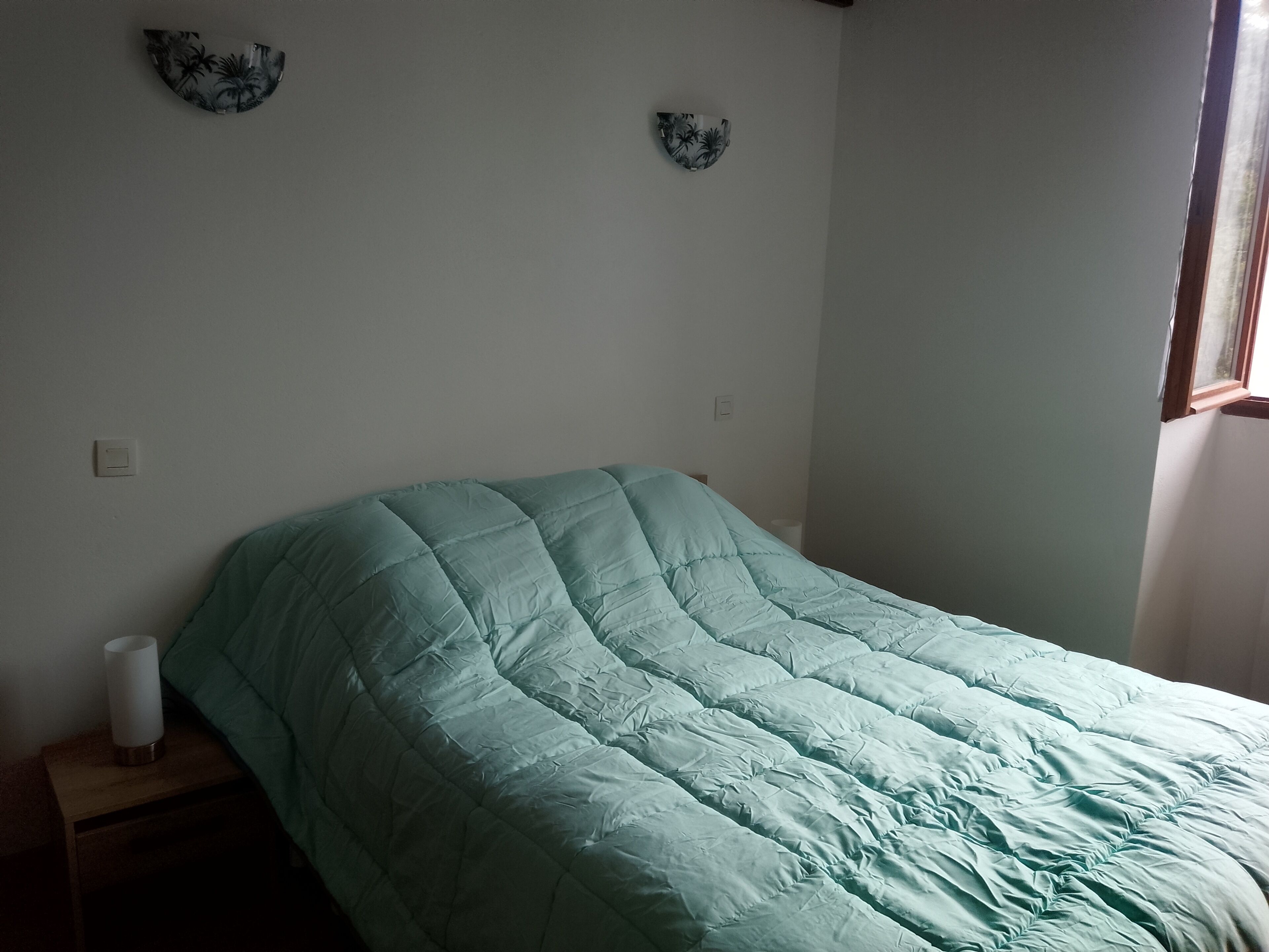 Una cama individual con colcha color turquesa, una mesita de noche con lámpara blanca y dos platos decorativos colgados en la pared.