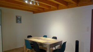 Uma sala de jantar com teto de madeira, uma mesa coberta com plástico protetor, quatro cadeiras e um poste preto.