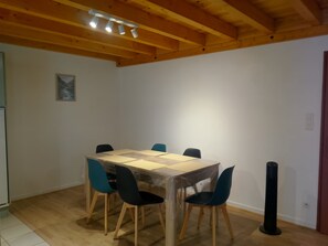 Ein Essbereich mit Holzbalkendecke, einem Tisch mit Schutzplane, vier Stühlen und einer schwarzen Stange.