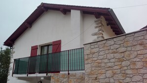 Uma casa de dois andares com varanda, parede de pedra e um vaso de flores.