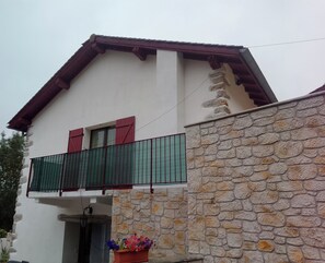 Ein zweistöckiges Haus mit Balkon, Steinmauer und einem Blumentopf.