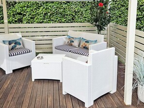 Un patio con mobili in vimini bianco, tra cui due sedie e un tavolino.