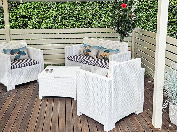 Eine Terrasse mit weißen Korbmöbeln, darunter zwei Stühle und ein kleiner Tisch.