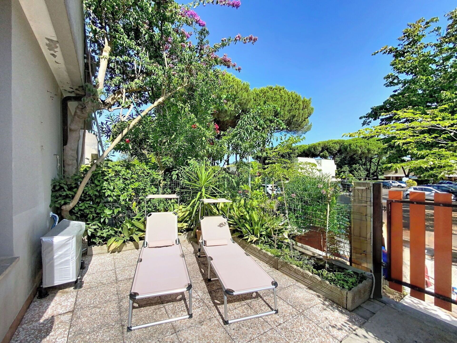 A patio with two sun loungers, a metal fence, and lush greenery.