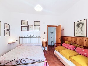 A bedroom with a bed, a bedside table, a lamp, a wooden wardrobe, and a door leading to another room. - Stunning  villa for 5 people with hot tub, WIFI, balcony, pets allowed and panoramic view (Rocca Sinibalda)