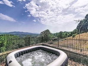 Ein Whirlpool, umgeben von einem Metallzaun, mit Blick auf ferne Berge und Grünflächen.