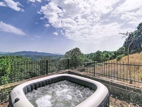 A hot tub surrounded by a metal fence, with a view of distant mountains and greenery.
