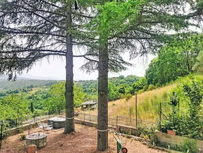 A natural landscape with a view of a hilly area, a fenced garden area with a bench, and a stone structure.
