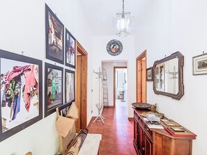 A hallway with framed pictures on the walls, a chandelier, and a wooden cabinet with items on top.