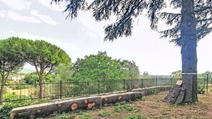 A fenced outdoor area with a stone pathway, trees, and a view of a distant building. - Beautiful  villa for 5 guests with hot tub, WIFI, balcony, pets allowed and panoramic view (Rocca Sinibalda)
