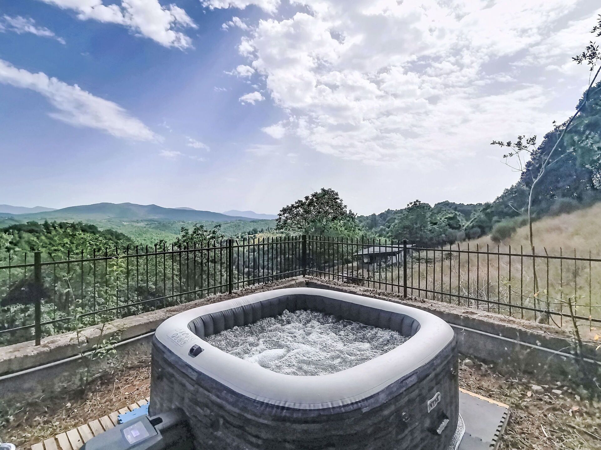 Een jacuzzi met een metalen reling, omgeven door een betonnen fundering, met op de achtergrond een bergachtig landschap en een heldere lucht.