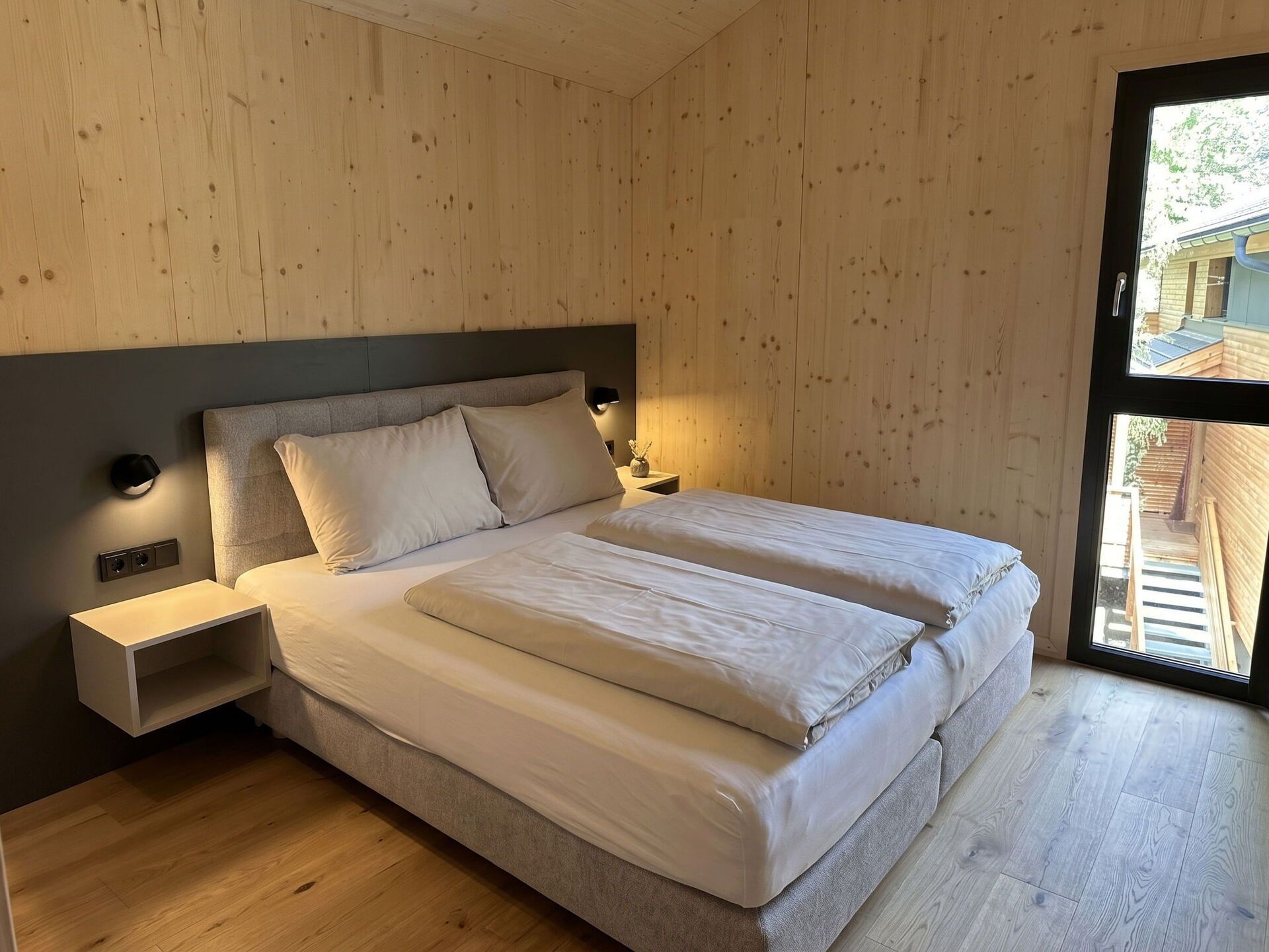 A modern bedroom with a wooden wall, a bed with two pillows, a bedside table, and a nightstand.