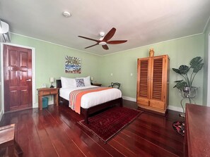 Un dormitorio con cama, mesita de noche, armario de madera, ventilador de techo y alfombra roja.