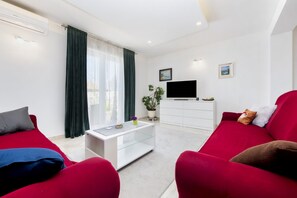 Ein modernes Wohnzimmer mit Flachbildfernseher, einer weißen Unterhaltungsecke und roten Sofas.