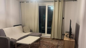 Ett vardagsrum med en soffa, ett soffbord, ett TV-bord och en mönstrad matta.