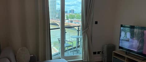 Una sala moderna con sofá, una mesita de centro, televisor y vistas a un paisaje urbano a través de un amplio ventanal.