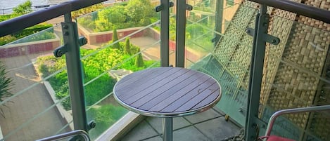 Un balcon avec une table ronde et deux chaises, donnant sur une rivière et un pont.