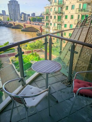 A balcony with a round table and two chairs, overlooking a river and a bridge. - Prime Vauxhall Location Stylish 2 Bedroom Riverside Apartment (London)