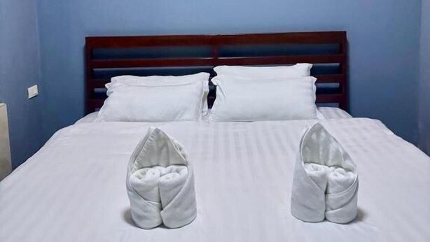 A hotel room with a bed, white linens, a wooden headboard, and a wall-mounted light fixture. - SCK Guesthouse (Vang Vieng)