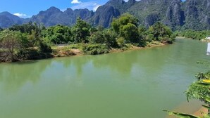 A river with a mountain backdrop, surrounded by greenery. - SCK Guesthouse (Vang Vieng)