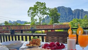 A table with food and drinks, a view of mountains, and a wooden fence. - SCK Guesthouse (Vang Vieng)