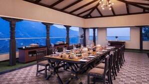 Comedor con una mesa larga dispuesta para una comida, ventanas amplias con vista a la montaña y estructura de techo de madera.