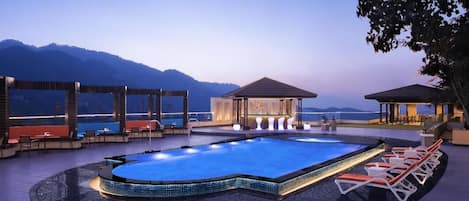 A swimming pool with lounge chairs, a covered seating area, and a view of the mountains.