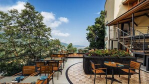 Un patio al aire libre con mesas y sillas, rodeado de follaje y vistas a montañas distantes.