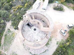 An aerial view of a circular building with a central open area, surrounded by a gravel path and greenery. - Sa Omu de S'Olia (Tertenia)