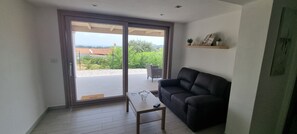 A living room with a sliding glass door leading to a balcony, a black sofa, a small table, and a shelf with decorative items. - Sa Omu de S'Olia (Tertenia)