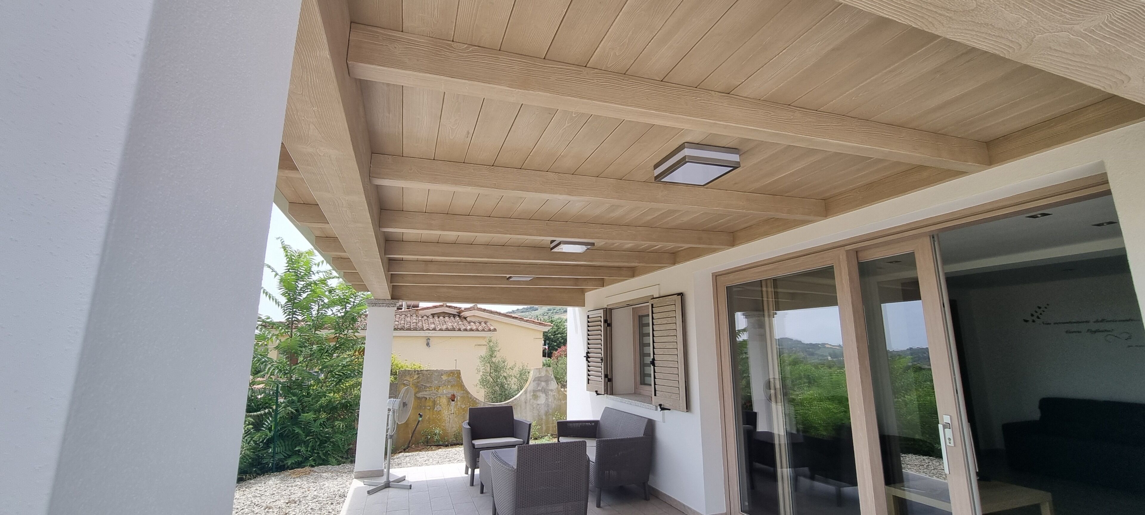 A covered outdoor area with a ceiling, a fan, and a seating arrangement.