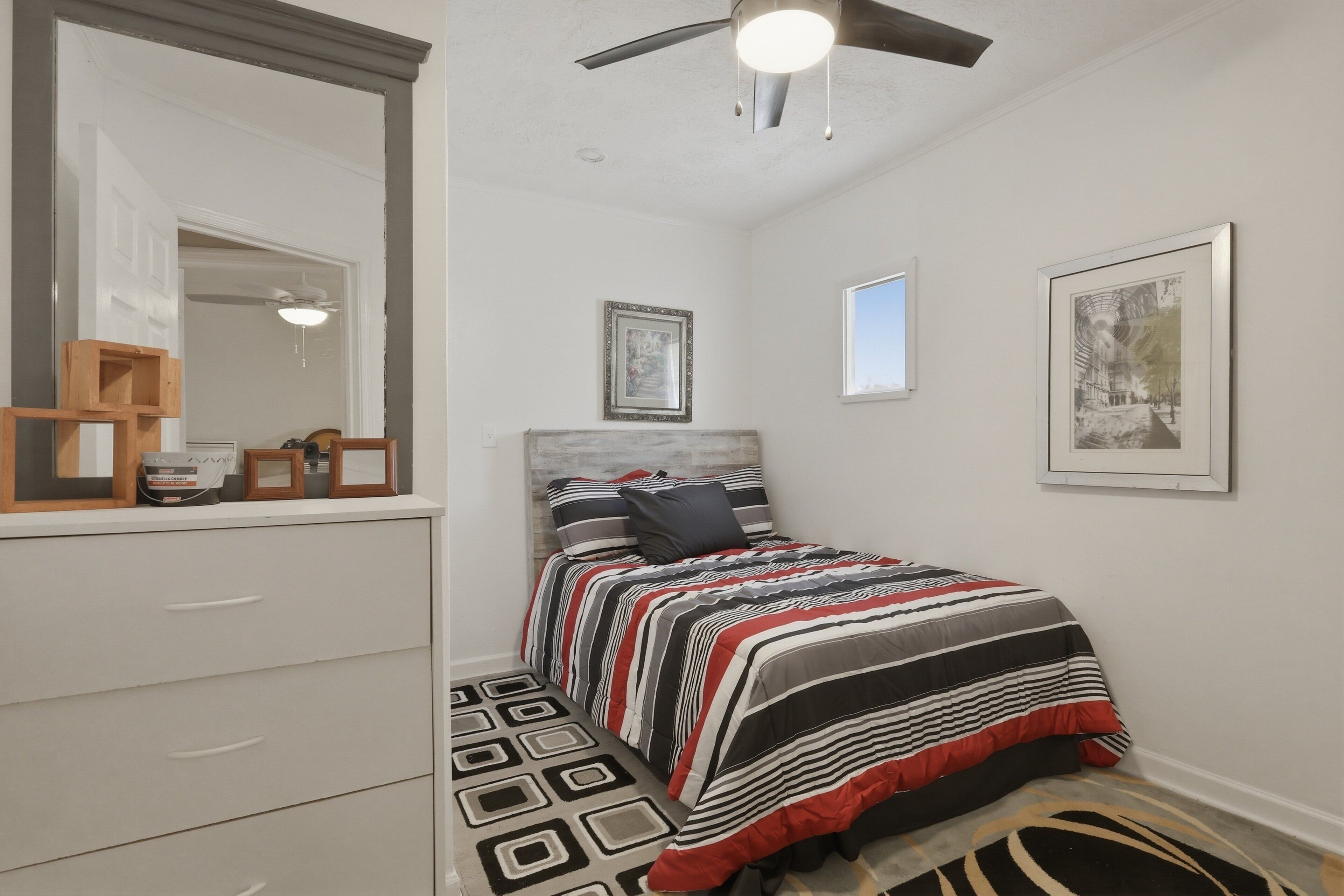 A bedroom with a bed, a dresser, a ceiling fan, and framed pictures on the walls.