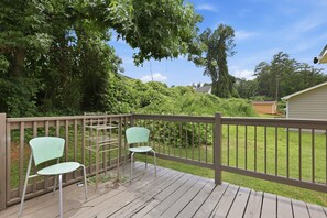 A wooden deck with two chairs and a metal table, surrounded by lush greenery and a house in the background. - Fireplace, Private Deck & 5 Bedroom Comfort 5 Home (Atlanta)