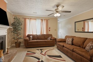 A living room with two sofas, a ceiling fan, a fireplace, and a large window with curtains. - Fireplace, Private Deck & 5 Bedroom Comfort 5 Home (Atlanta)