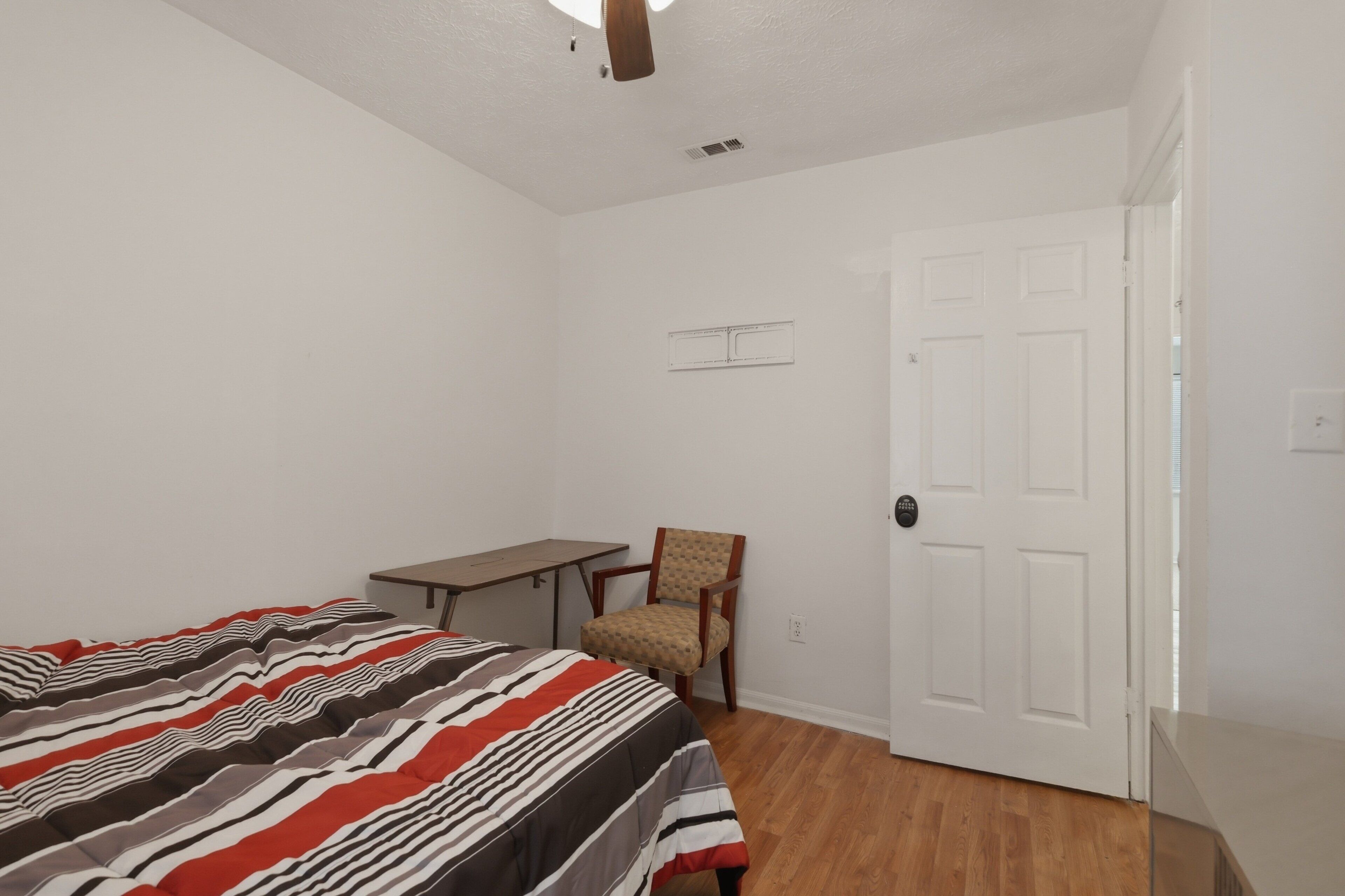 A bedroom with a bed, a desk, a chair, and a door.