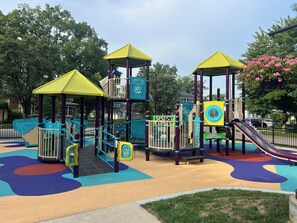 Ein Spielplatz mit verschiedenen Spielgeräten, darunter eine Rutsche und Kletterbereiche, umgeben von einem bunten Spielbereich.