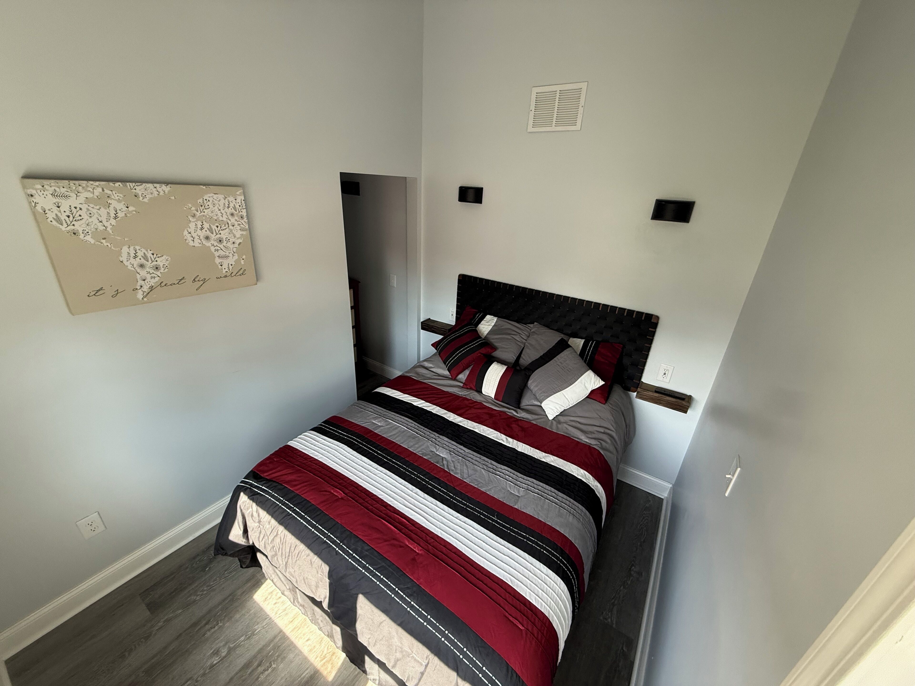 Un dormitorio pequeño y ordenado, con una cama individual, un mapa en la pared y una rejilla de ventilación sobre la cama.