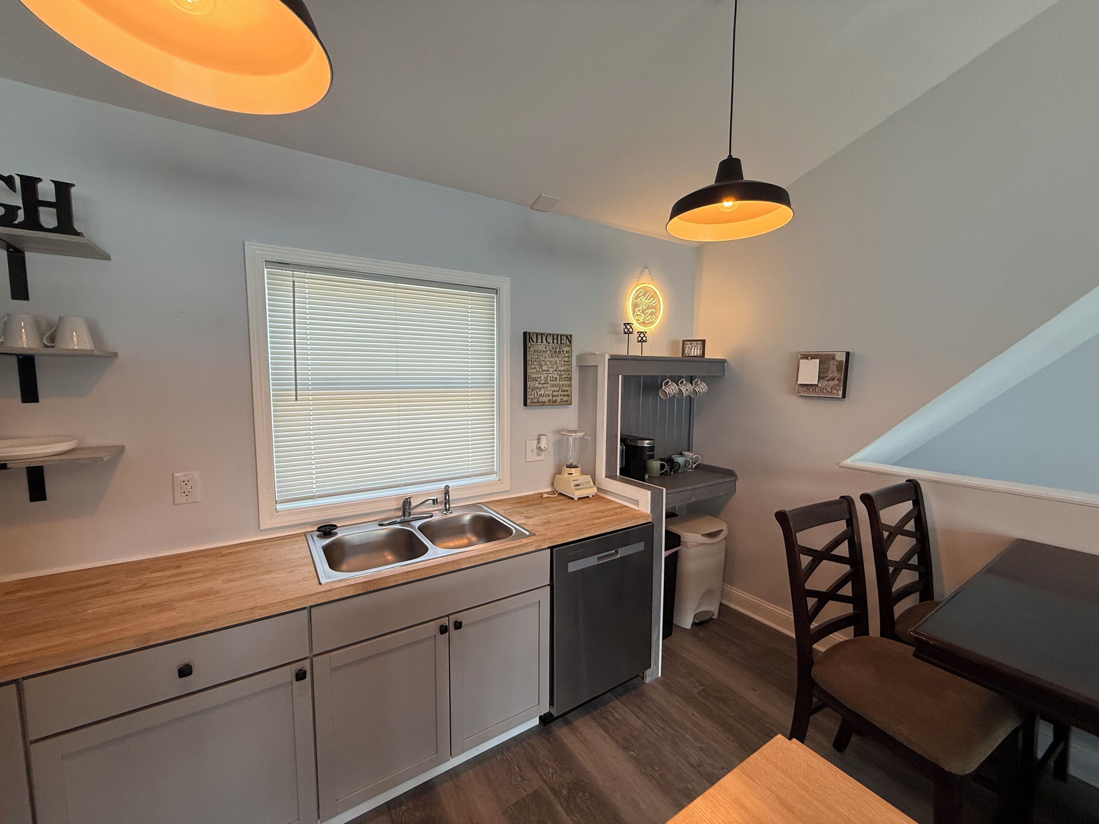 A modern kitchen with a built-in dishwasher, a window with blinds, and a dining area with a table and chairs.